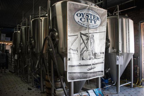 Interior of a brewery featuring large stainless steel fermentation tanks and a banner for Oyster City Brewing Company.