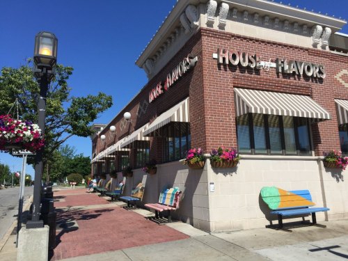 A brick building with "House of Flavors" sign, colorful benches, and flower baskets under a clear blue sky.