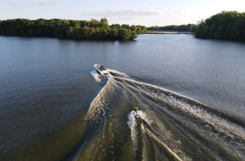 Aerial view of a boat towing a water skier on a calm lake surrounded by lush greenery.
