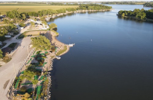 Aerial view of a calm river with boats, green trees, and a park area along the shore.