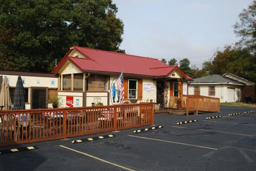 A small building with a red roof, wooden deck, and parking lot, featuring signs and decorations outside.