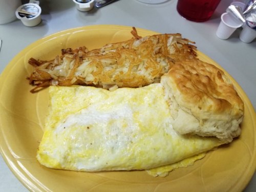 A plate with a fluffy omelet, crispy hash browns, and a biscuit, served on a yellow dish.