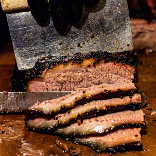 A close-up of sliced brisket being cut with a cleaver, showcasing its smoky, tender layers.