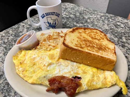 A plate with an omelet, bacon, hash browns, toast, and a cup of coffee in the background.