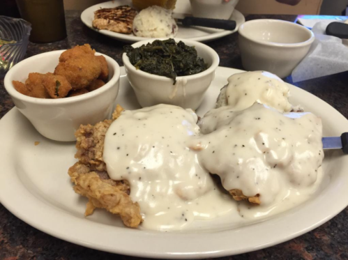 A plate of fried chicken smothered in white gravy, served with collard greens and fried okra in small bowls.