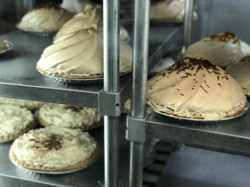 A display of various pies on metal shelves, featuring meringue-topped pies and cream-filled varieties.