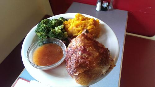 A plate with roasted chicken, broccoli, mashed sweet potatoes, and a small bowl of sauce.