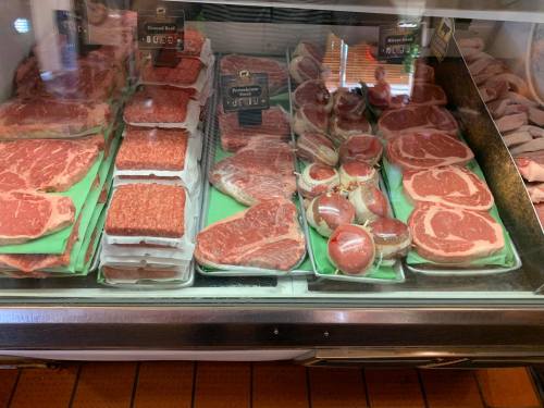 A display case filled with various cuts of meat, including ground beef and ribeye steaks, neatly arranged on green trays.