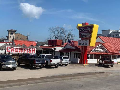 A restaurant with a red roof and sign, featuring a "Crawfish" banner, surrounded by parked trucks.
