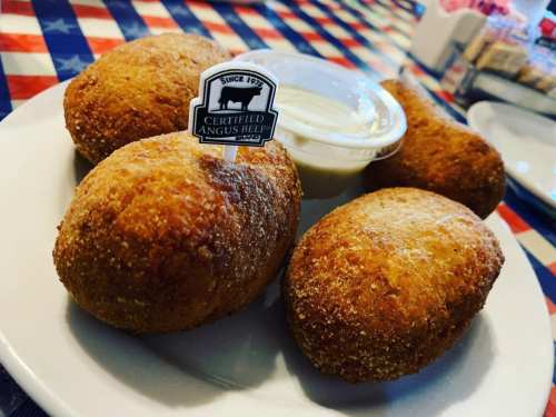 A plate of four golden-brown, breaded rolls with a small cup of dipping sauce and a tag reading "Certified Angus Beef."