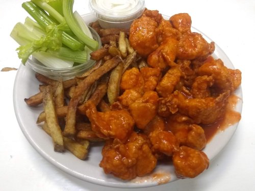 A plate of crispy fried chicken in spicy sauce, served with celery sticks and a side of fries.