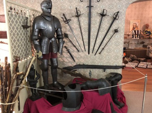 A display of medieval armor and weapons, including a suit of armor, swords, and various tools, in a museum setting.