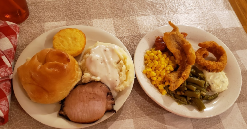 A plate of food featuring sliced meat, mashed potatoes with gravy, corn, green beans, fried fish, and a roll.