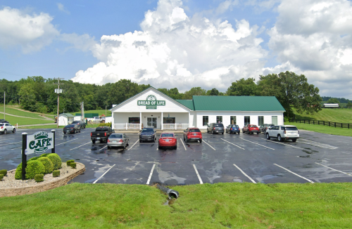 A building labeled "Bread of Life" with a green roof, surrounded by parked cars and grassy areas under a cloudy sky.