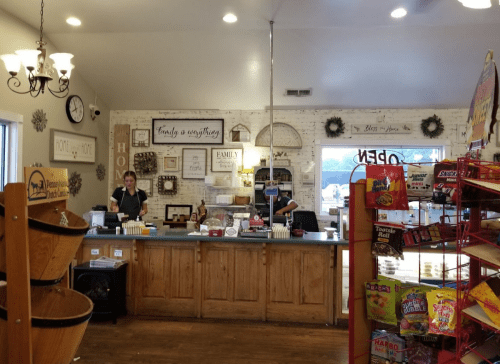 A cozy shop interior with two employees at the counter, shelves of snacks, and decorative wall signs.