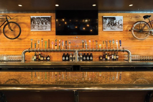 A bar with a wooden wall, featuring a variety of beer taps, bottles, and vintage bicycle decor.