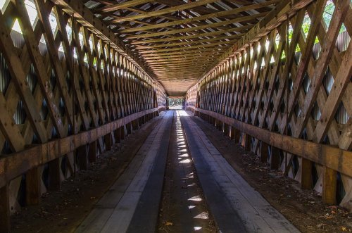 A covered wooden bridge interior with a lattice design, featuring light streaming through and casting shadows on the floor.