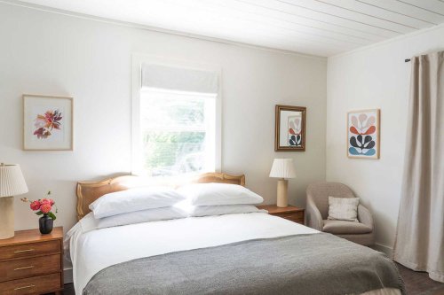 Bright, cozy bedroom with a large bed, two lamps, artwork on the walls, and a comfortable chair in the corner.