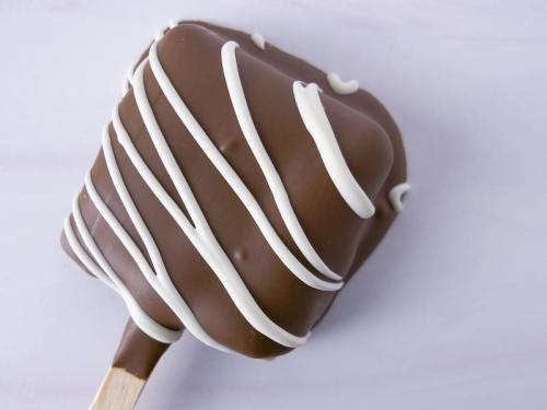 A chocolate-covered ice cream bar drizzled with white chocolate on a stick, set against a light background.