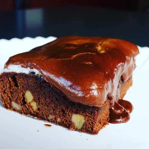 A rich chocolate cake with a glossy frosting, featuring nuts peeking through the moist, dense texture.