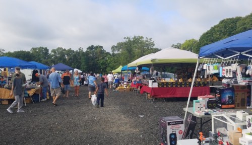 A bustling outdoor market with various stalls, colorful tents, and people browsing goods on a cloudy day.