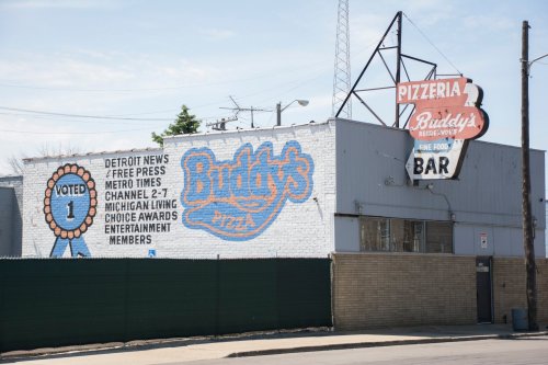 A brick building with a mural for Buddy's Pizza, featuring awards and a sign for the pizzeria and bar.
