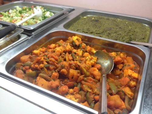 A buffet display featuring a vegetable curry, a green dish, and a fresh salad in metal trays.