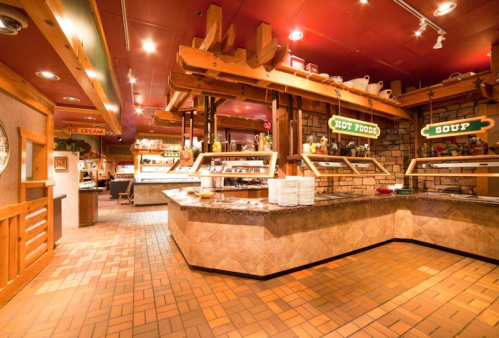 A cozy buffet restaurant with wooden decor, featuring food stations for hot dishes and soup. Warm lighting enhances the atmosphere.
