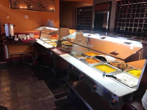 A buffet setup with various dishes in metal trays, including rice, meats, and sides, in a warm restaurant setting.