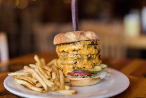 A towering cheeseburger with multiple patties, melted cheese, and toppings, served with a side of crispy fries.