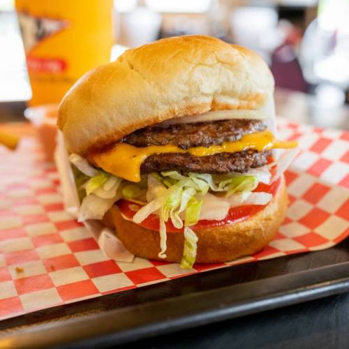 A juicy cheeseburger with two patties, lettuce, tomato, and onion on a toasted bun, served on a checkered tray.