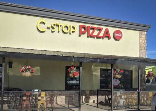 Exterior of C-Stop Pizza restaurant with colorful signage and outdoor seating under a clear blue sky.