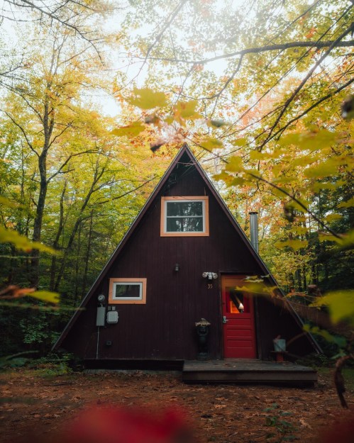 A cozy A-frame cabin surrounded by vibrant autumn foliage in a serene forest setting.