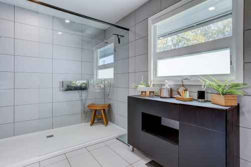 Modern bathroom featuring a glass shower, a wooden stool, and a sleek black vanity with plants and decor.