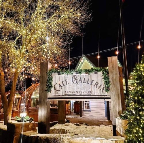 A warmly lit café entrance adorned with festive lights and greenery, set against a night sky.