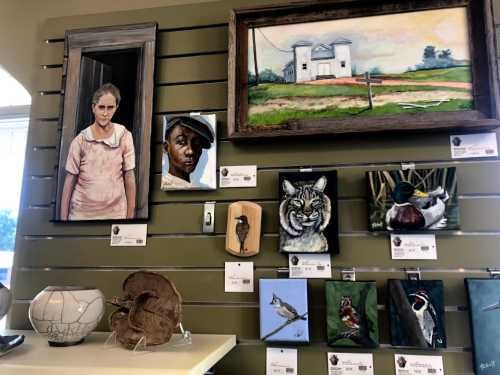 A gallery wall displaying various artworks, including portraits and animal paintings, with labels and price tags.