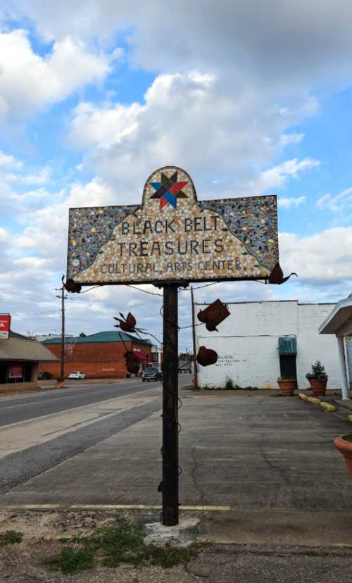 Sign for Black Belt Treasures Cultural Arts Center, featuring a colorful design, set against a cloudy sky.