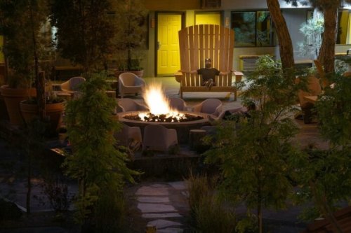 A cozy outdoor fire pit surrounded by chairs, with a large wooden chair in the background and soft lighting.