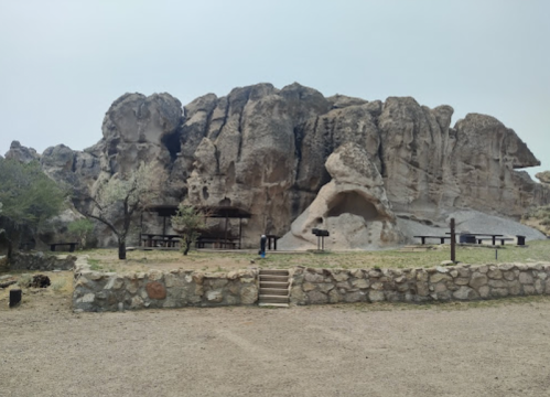 Rocky cliffside with picnic tables and a stone wall in a natural setting, under a cloudy sky.