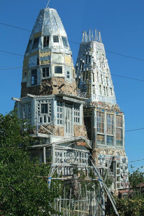 Unique architectural structure featuring two tall towers adorned with various materials and intricate designs against a blue sky.