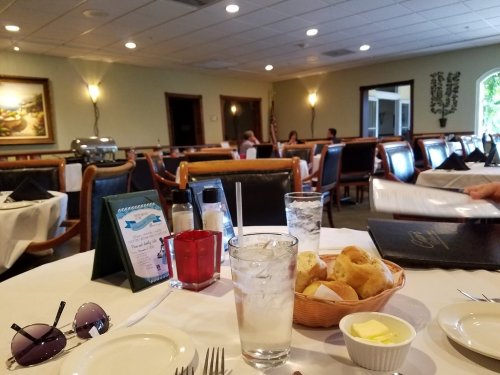 A restaurant interior with tables set for dining, featuring water glasses, bread rolls, and a menu on the table.