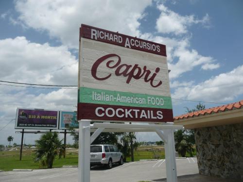 Sign for Richard Accursio's Capri, featuring Italian-American food and cocktails, with a cloudy sky in the background.