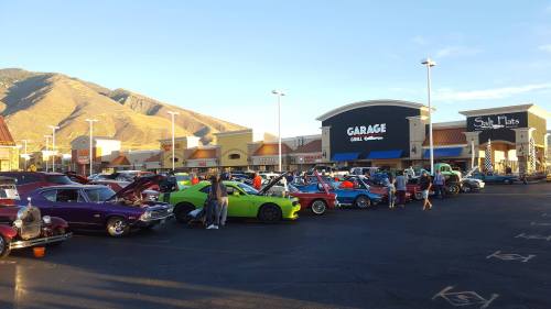 A car show featuring colorful classic cars parked outside shops, with mountains in the background under a clear sky.