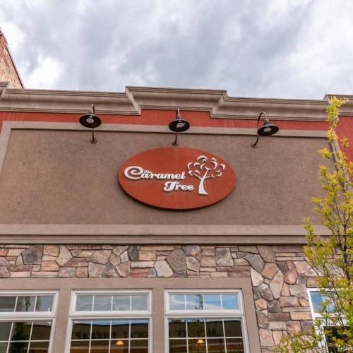 Sign for "The Caramel Tree" on a stone building exterior under a cloudy sky.