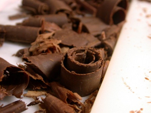 Close-up of chocolate shavings, featuring curled and layered pieces on a white surface.