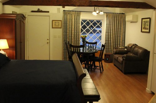 Cozy room featuring a bed, dining table, and seating area with a window and warm lighting.