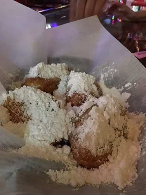 A plate of fried dough balls dusted with powdered sugar, served in a paper wrapper.