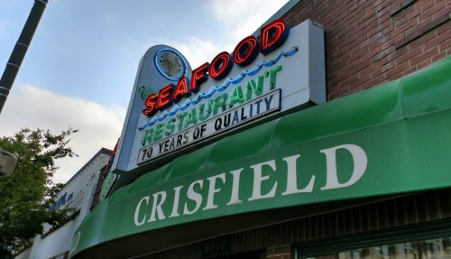 Sign for Crisfield Seafood Restaurant, featuring bright neon letters and a green awning, emphasizing quality.