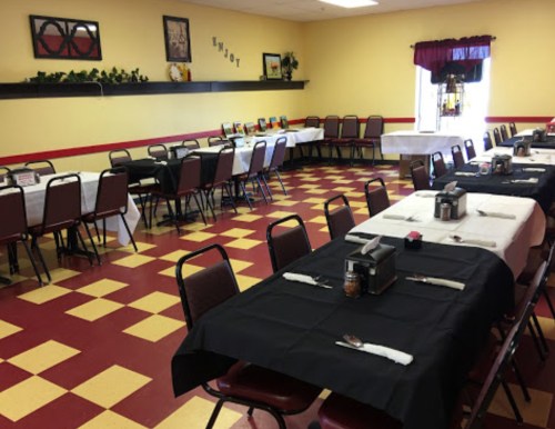 A spacious dining area with tables set in black and white linens, red chairs, and a checkered floor.