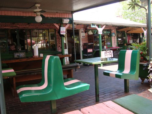 Outdoor dining area with green and pink chairs and tables, surrounded by plants and a casual, inviting atmosphere.
